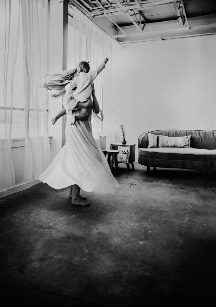 Newborn Photographer, a woman in a long skirt dances while holding baby, her dress twirls within the room