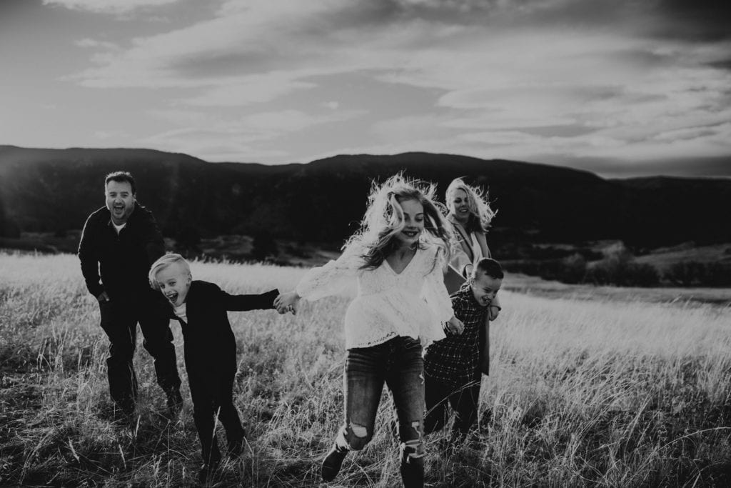 Family Photographer, two children pull their parents through a dry grass meadow