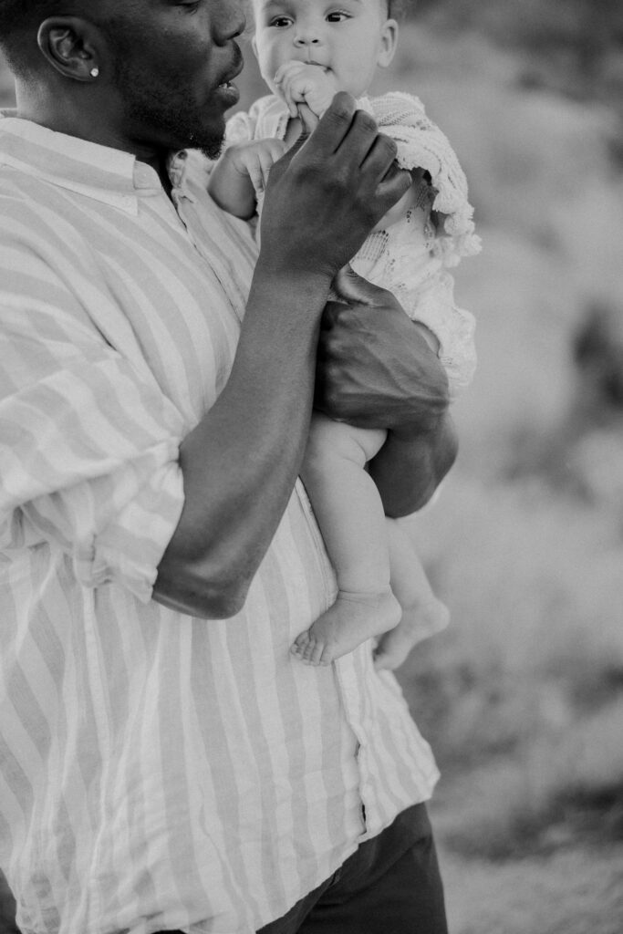 Family and Newborn Photographer, a father holds his young baby in his arms outside